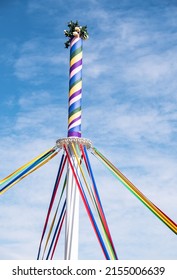 A vertical shot of a pole with colored ribbons and flowers on a traditional Maypole dancing day