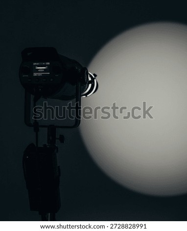 Vertical shot of a professional continuous studio light for photo and video shooting, casting a round light spot on the wall. Minimal modern lighting concept.