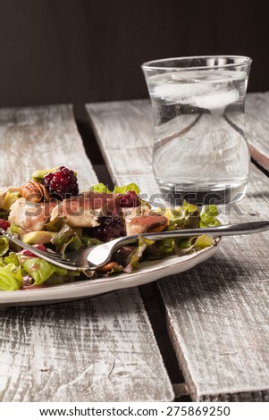 Vertical shot of raspberry pecan grilled chicken avocado salad on an old weathered barn wood table with a clear glass of water