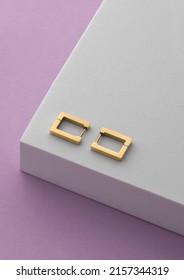 Vertical shot of rectangle earrings pair on white podium on purple background with copy space