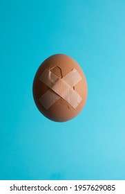 A Vertical Shot Of A Red Cracked Egg Stitched By Band Aid Cross On Bright Blue Background With Copy Space