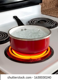 Vertical Shot Of A Red Pan Of Boiling Water On Top Of A Stove With The Burner Turned To High.