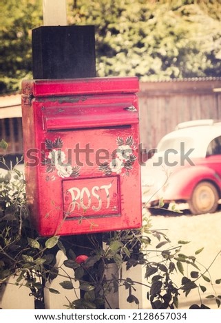 A vertical shot of a red post box of a little teashop with a vintage car in the background