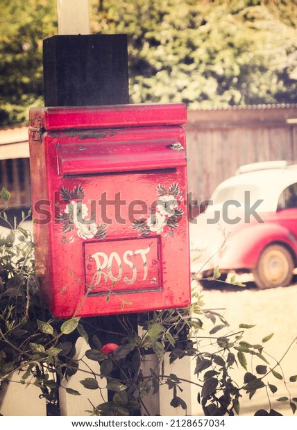A vertical shot of a red post box\
of a little teashop with a vintage car in the\
background