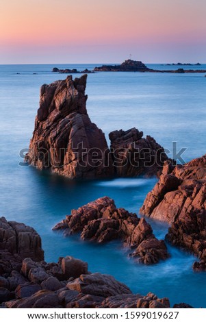 A vertical shot of rock formations in the beautiful clear blue sea in Guernsey