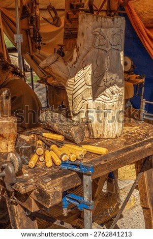 A vertical shot of a rustic carpenter's workbench featuring a hand-carved wooden owl sculpture, professional carving chisels, and traditional woodworking tools at a craft fair.