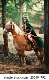 Vertical Shot Of A Sexy Brave Female Elf Archer In A Green Cape Riding Her Horse In The Woods Danger Dangerous Skilled Fighter Weapon Armed Mysterious Forest Hiding Hunting Costume Character Creature.