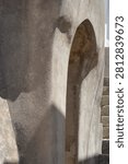 A vertical shot shows a rustic arched entrance built into a rough concrete wall under strong sunlight creating geometric shadows