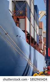 Vertical shot of the side of a container ship with cargo containers moored at a commercial dock.