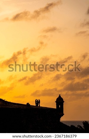 Vertical shot of silhouettes of people near the walls of El Morro Fort at golden sunset, old San Juan, Puerto Rico