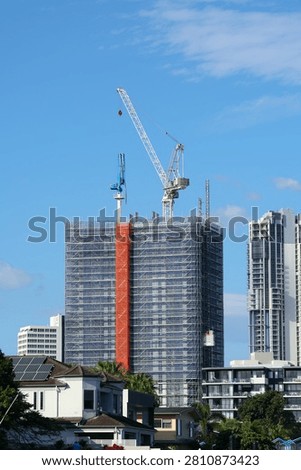 Vertical shot of skyscraper construction site with crane, scaffolding, and orange safety netting.