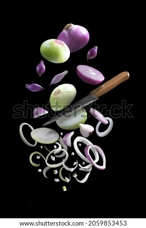 A vertical shot of sliced falling onion with a knife on black background