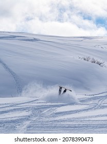A vertical shot of a snowboarder falling down on a snowy off-piste ski slope