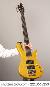 Vertical shot of a strong man hand holding a bass guitar with five chords. Studio shot over light grey background.