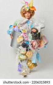 Vertical Shot Of Surprised Female Volunter Cleans Up Earth From Contamination Makes Costume From Plastic Garbage Carries Rubbish Bin Worries Because Of Global Problem Isolated Over Grey Background