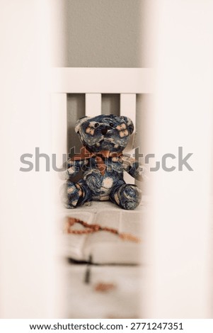 A vertical shot through crib bars of a unique plush teddy bear featuring the Starry Night painting pattern, sitting in a white wooden crib