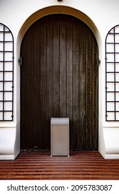 A vertical shot of a trashcan in front of a wooden door, on a brick floor