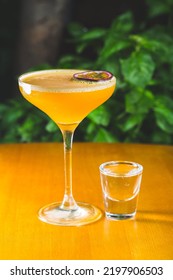 A Vertical Shot Of A Tropical Drink Served With Passionfruit Slice And A Glass Of A Syrup