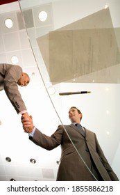 Vertical Shot Of Two Businessmen Shaking Hands After Signing Paperwork On Glass Table Seen From Low Angle View Through The Glass.