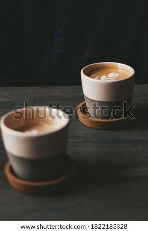 A vertical shot of two ceramic cups of foamy caffe latte on a wooden table