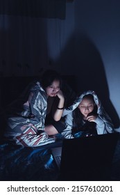 A Vertical Shot Of Two Hispanic Young Women At A Sleepover Watching Movies At Dark On A Laptop