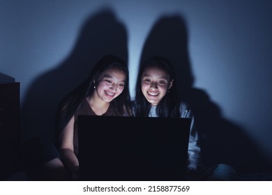 A Vertical Shot Of Two Hispanic Young Women At A Sleepover Watching Movies At Dark On A Laptop