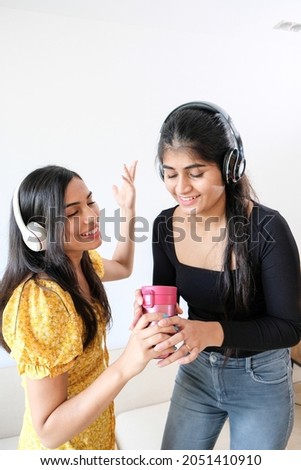 A vertical shot of two young girls dancing in a room with headphones and holding a cup