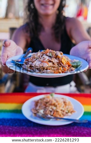 Vertical shot of an unrecognizable woman offering a plate of freshly made Pad Thai at a street food stall. Thai asian food ration.