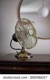 Vertical shot of vintage table fan on dresser with mirror in background and clock
