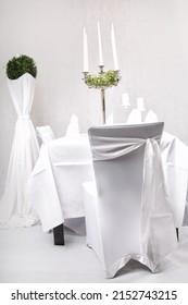 A Vertical Shot Of A White-themed Romantic Table Set Up With Candles On A Stand