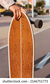 A Vertical Shot Of A Woman With A Shirt Holding A Longboard On A Bike Path Towards The Beach. Young Girl Holding A Skate And Casting Her Shadow On The Paved Bike Path Between Palm Trees.