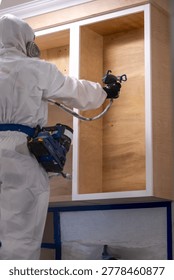 Vertical shot of Worker using a spray gun to apply paint or coating cabinet during renovation.