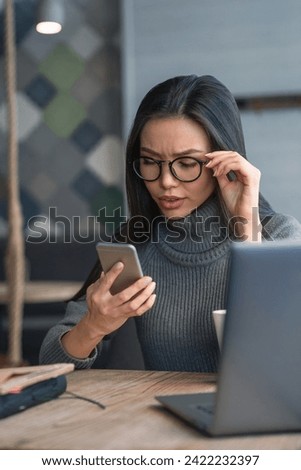 Vertical shot of working process. Young business woman with full concentration checking her mobile phone sitting on a table at coworking. Remote job, loan, mortgage, financial issues