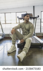 A Vertical Shot Of A Young Attractive Male In A Sweat Suit Posing Sitting On A Treadmill