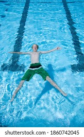 Vertical Shot Of A Young Boy In Swimming Trunks Floating In A Swimming Pool.