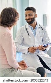 Vertical shot of young happy cheerful Indian medical worker therapist in white doctor's robe having appointment consulting older female patient in modern clinic hospital. Medical healthcare concept. - Shutterstock ID 2033522243