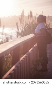 A Vertical Shot Of A Young Hispanic Female Standing Near A Wall And Enjoying The View Of The Sunset