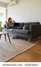 Vertical Shot Of Young Man Drinking Coffee From Mug While Working With Laptop On The Sofa