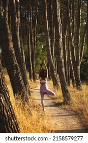 A vertical shot of a young woman doing yoga in a narrow pathway in a forested area