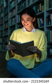 Vertical Shot Of The Young Woman Reading Book At The Library And Smiling Toothy. Brunette Lady Studying At The High School. Stock Photo 