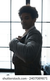 Vertical side view image of elegant african american businessman getting ready for business meeting, putting on and buttoning his jacket standing against big window, looking at camera
