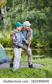 Vertical Side View Portrait Of Loving Father Teaching Son Fishing While Enjoying Camping Trip Together