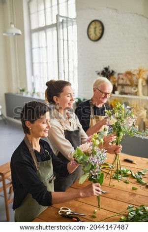 Vertical side view portrait of three florists arraigning flower compositions in cozy workshop
