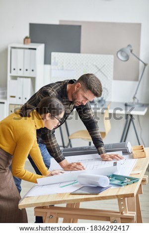 Vertical side view portrait of two architects cdrawing blueprints while working in office together