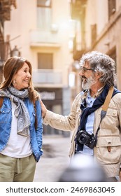 Vertical. Smiling elderly couple having fun chatting standing outdoors in city. Pensioners enjoying sightseeing tour together on street in spring. Mature marriage relationship and retiree vacation.