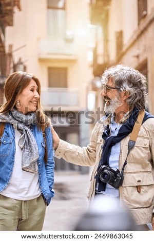 Vertical. Smiling elderly couple having fun chatting standing outdoors in city. Pensioners enjoying sightseeing tour together on street in spring. Mature marriage relationship and retiree vacation.