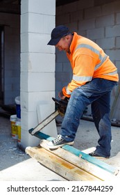 Vertical Smiling Worker Man In Orange Protective Coverall Using Chainsaw Cutting Wood Piece And Metal Tubes. Build House