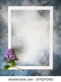 Vertical spring composition with a white frame and a fresh sprig of lilac on a blue textured background with copy space for lettering and text.  Empty place for inspirational text ore lovely quote