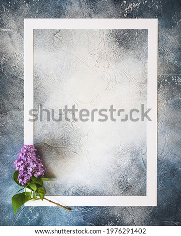 Vertical spring composition with a white frame and a fresh sprig of lilac on a blue textured background with copy space for lettering and text.  Empty place for inspirational text ore lovely quote
