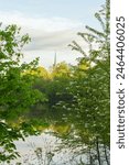 
Vertical spring view of the Cap-Rouge river and spire of the 1859 Saint-Felix-de-Valois church seen through foliage, Quebec City, Quebec, Canada 